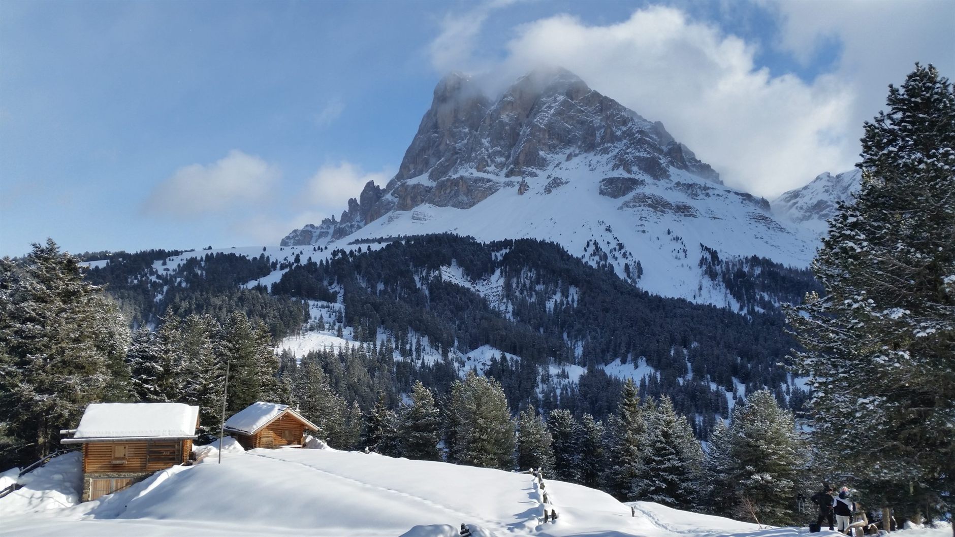Besneeuwde houten almhutten en dennenbossen onder een Dolomietentop in Zuid-Tirol